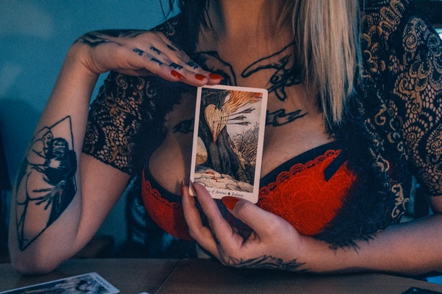 Žena v erotickom oblečení si pred prsiami drží tarotovú kartu.jpg