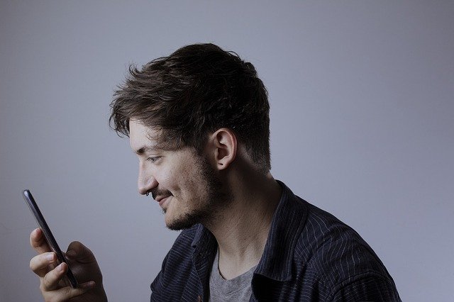 Muž s piercingom v nose pozerá do mobilného telefónu