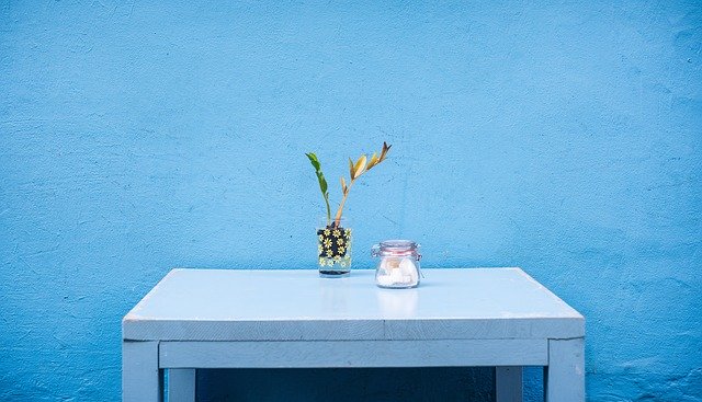 Stôl pred modrou stenou, váza s kvetom a dóza so sladkosťami